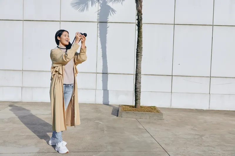 Woman outdoors holding camera and shooting, daylight scene, casual street fashion, urban backdrop, candid photography moment capturing movement and lifestyle expression