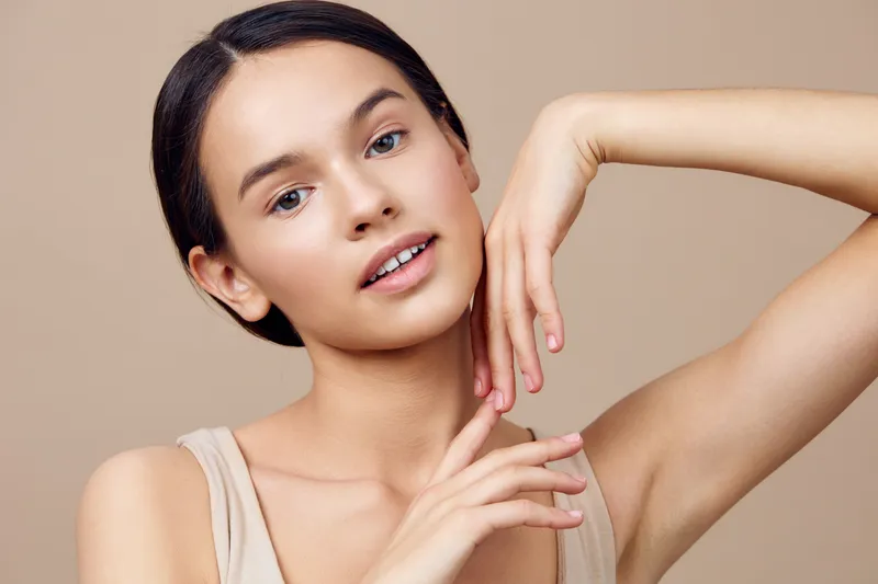 Young woman with natural makeup and elegant pose, showcasing beauty and confidence against a soft beige background