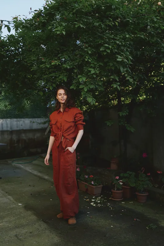 Vibrant lifestyle moment with a woman in a red dress outdoors, relaxed pose, soft smile, sunlit scene, leafy background, natural colors, casual elegance