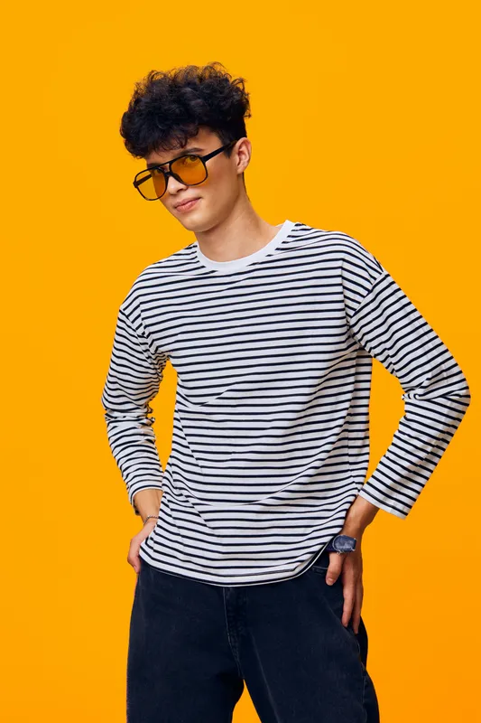 young man in striped shirt wearing yellow sunglasses posing confidently against bright orange background with casual style and modern hairstyle