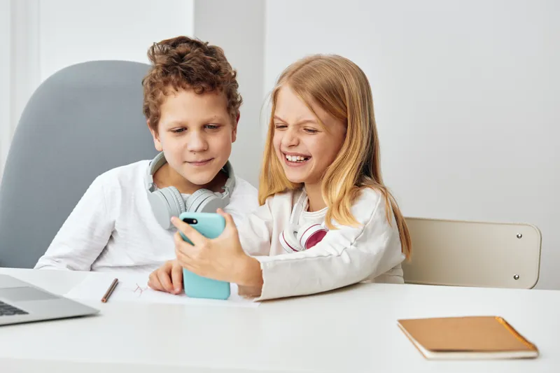 Счастливые мальчик и девочка европеоидной расы учатся дома, используя ноутбуки и наушники для электронного обучения