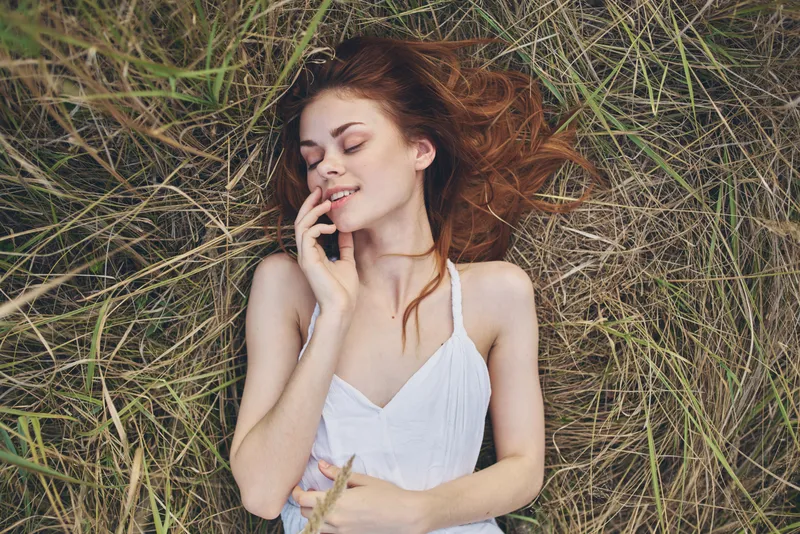 Женщина в белом платье лежит на траве, отдыхая на природе