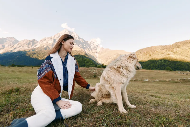 Woman and dog sitting in a mountain meadow pet portrait, outdoor nature scene with fluffy canine companion on grass, relaxed moment of bonding and scenic landscape.