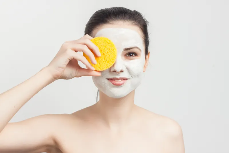 Брюнетка протирает лицо косметическими спонжами, обрезанный вид