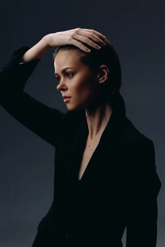 thoughtful woman in black clothing with contemplative expression against dark background