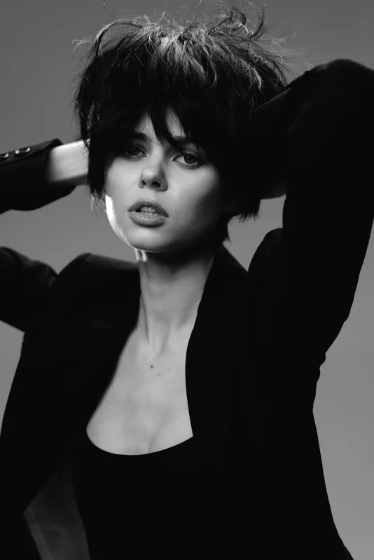 Black and white portrait of a fashionable woman with messy hair wearing a black outfit and expressive pose.