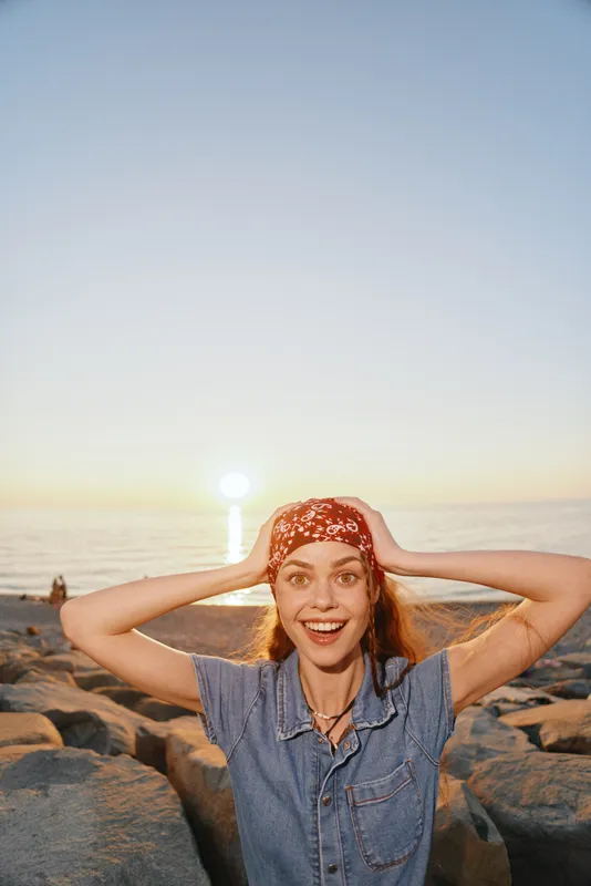 lifestyle woman in modern boho-western denim street style smiling with excitement during sunset at rocky beach, film color warms the scene with natural light