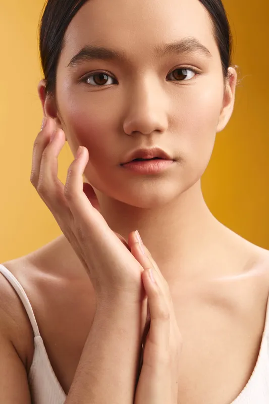 Asian woman gazes softly at the camera, a close up portrait with warm lighting, serene expression, smooth skin, calm confidence, minimal makeup, simple styling, creating a gentle inviting mood.