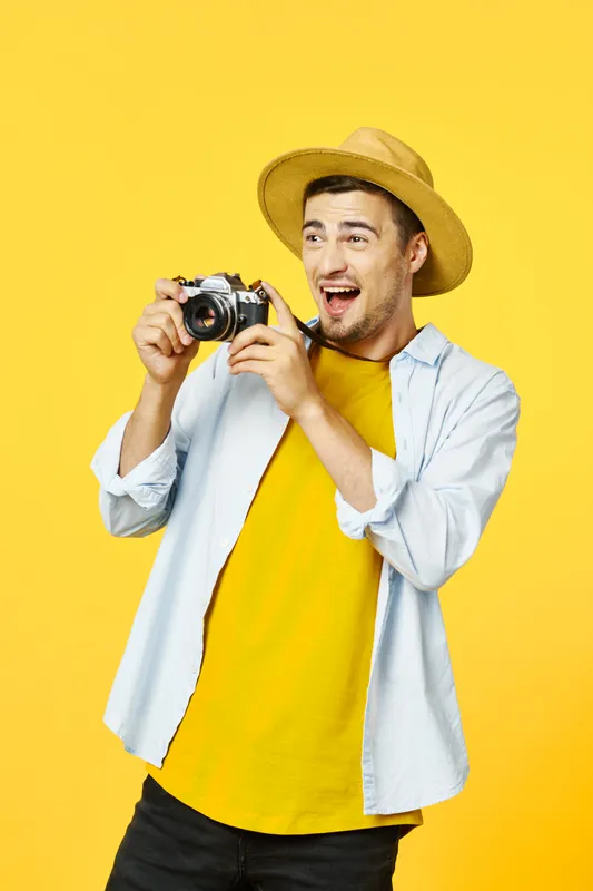 Счастливый фотограф с камерой в руках отводит взгляд в сторону на изолированном фоне