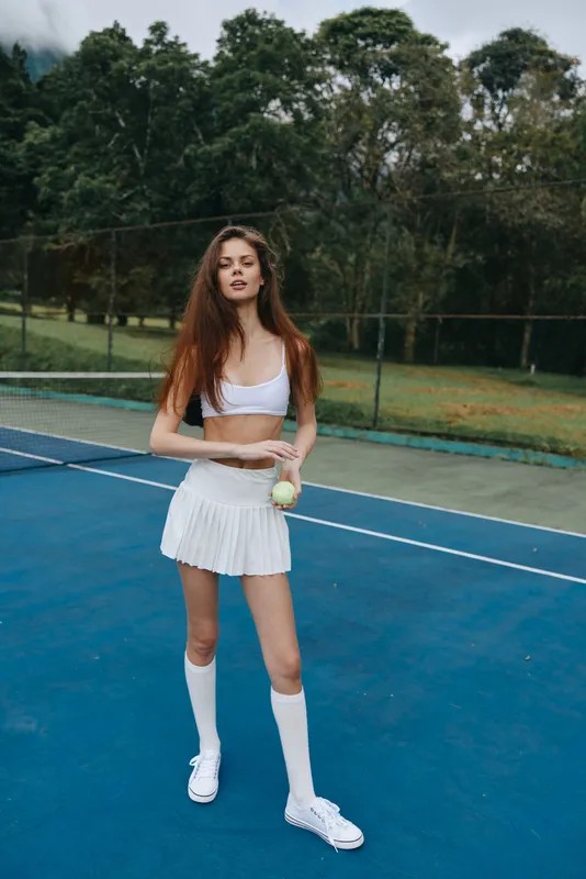 Young athletic woman in sportswear on tennis court, showcasing confidence and energy, surrounded by greenery, perfect for fitness and sports themed projects