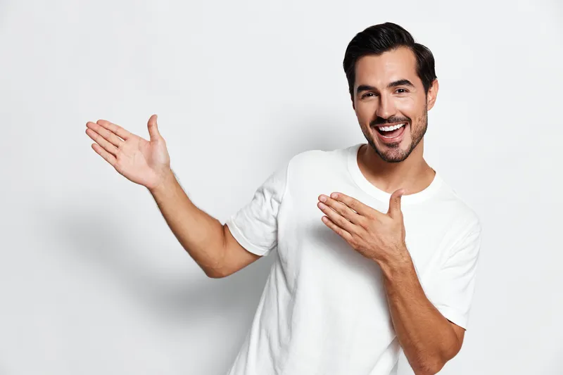 Full body smiling cheerful young man wearing white t-shirt looking at camera pointing with hands isolated on plain solid light background studio portrait. Lifestyle concept