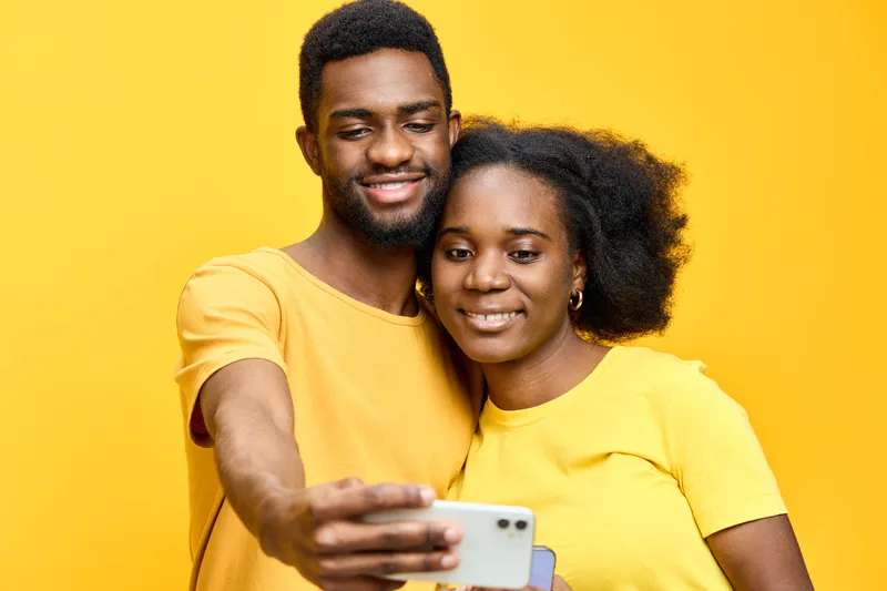 Happy couple taking a selfie against a vibrant yellow background, wearing matching yellow t shirts, capturing joyful moments and love for each other