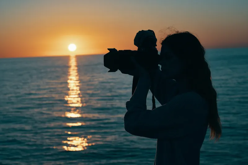 Женщина-фотограф с камерой на закате у моря на фоне природного пейзажа