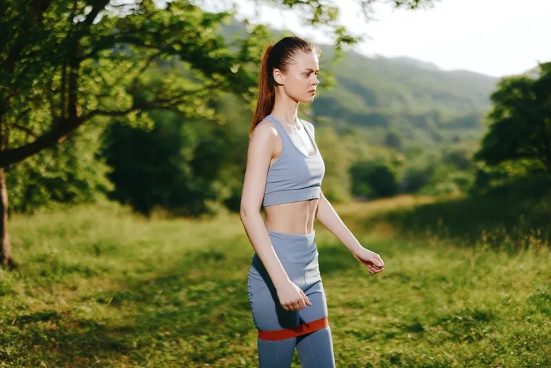 Young athletic woman in stylish blue activewear, walking outdoors in a sunny forest, embodying a healthy lifestyle and fitness concept
