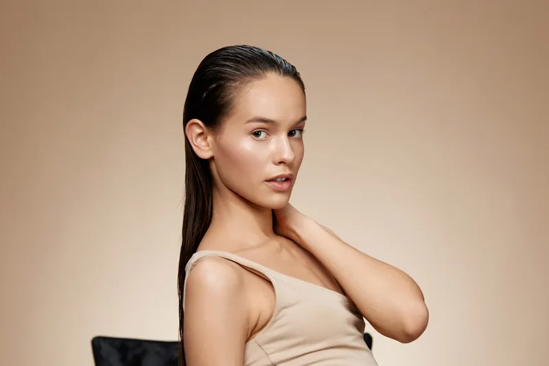 Elegant young model with wet hair poses gracefully against a neutral background, showcasing beauty and skincare concepts
