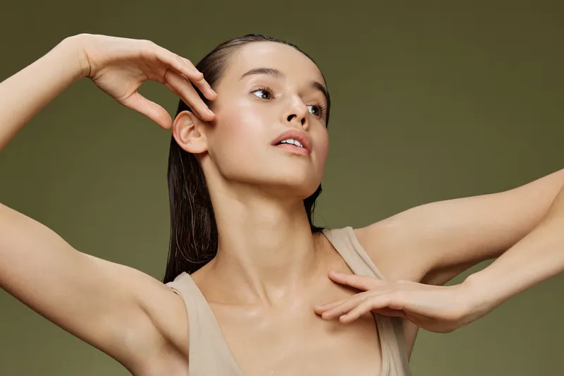 A graceful young woman posing against a soft green background, showcasing her serene expression and elegant posture in neutral clothing, representing beauty and self care