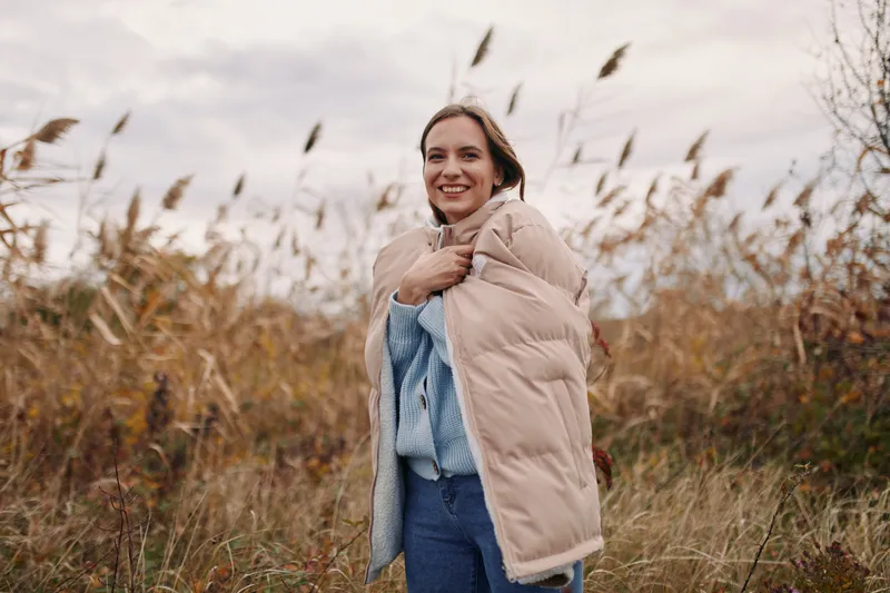 A candid, authentic portrait of a woman outdoors, wrapped in a warm coat, conveying real emotion and everyday truth under soft autumn light.