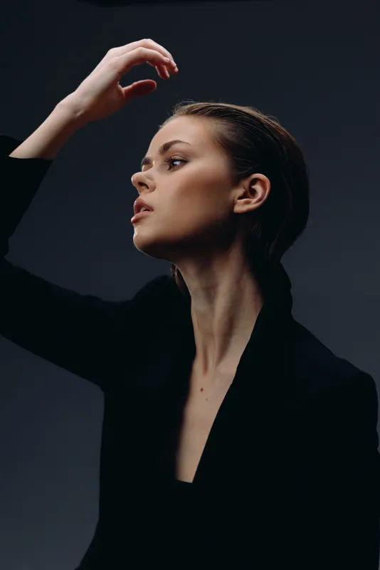 Elegant woman with serious expression posing against dark background in minimalist style and black outfit