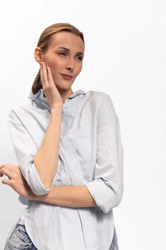 Young woman in casual shirt touches her face with a thoughtful expression. Bright studio with white background. Concept of contemplation, beauty, and natural emotion.