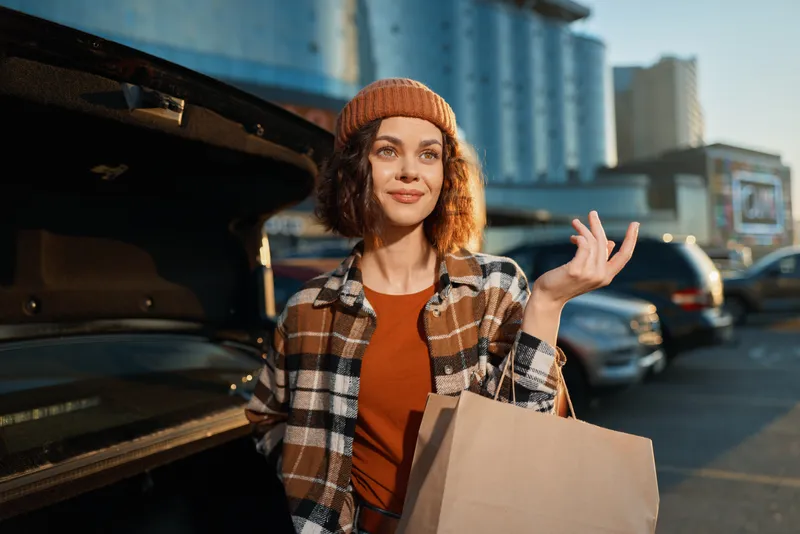 woman shopping by car trunk with paper bag in urban parking lot, candid lifestyle portrait at golden hour glow, authenticity and emotional storytelling conveying mindful living and modern city style