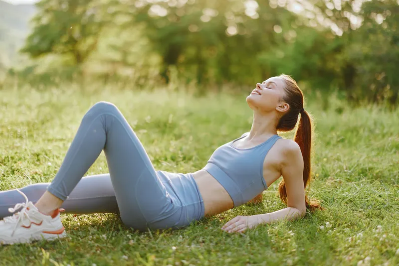 Young woman in athletic wear enjoying sunny outdoor yoga, promoting healthy lifestyle with bright colors and serene nature background