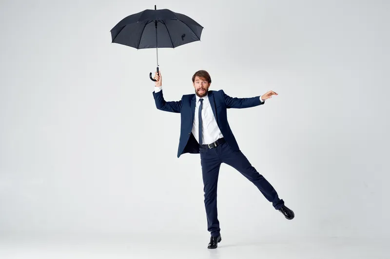 Мужчина в костюме с зонтом в руках, демонстрирующий защиту от дождя и элегантный стиль, в полный рост