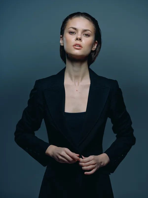 Confident woman in black blazer posing with serious expression in a dark studio setting