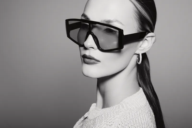 Stylish Caucasian woman with pale skin wears large black sunglasses and a white knit sweater. Concept of fashion, elegance, beauty, and modern minimalism in studio lighting.