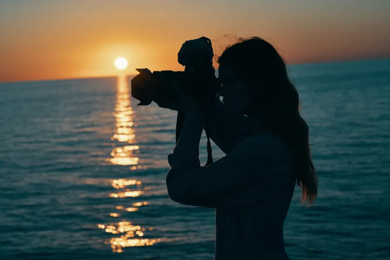 Женщина-фотограф с камерой на закате у моря на фоне природного пейзажа
