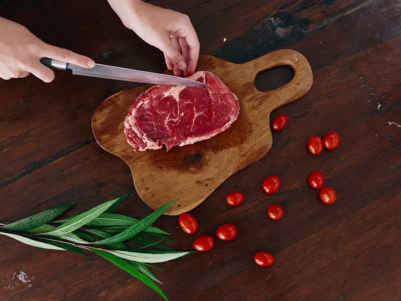Женщина с ножом в руке нарезает свежее мясо стейка для жарки на кухне