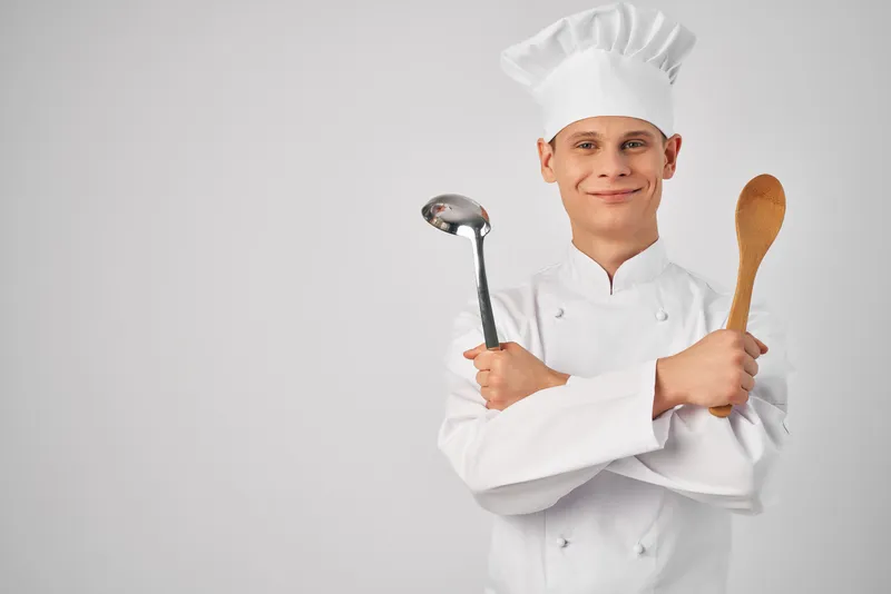 Повар с половником и деревянной ложкой в руках занимается кухонной работой