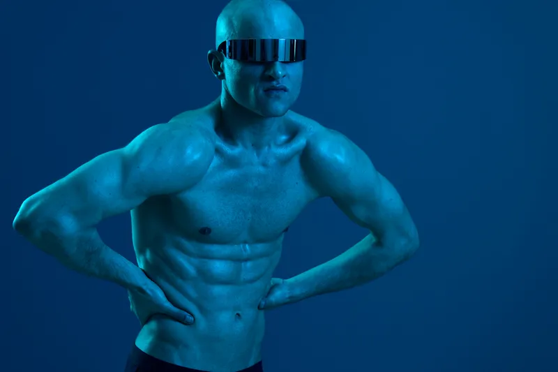 Strong man with sunglasses posing in a vibrant blue light, showcasing a muscular physique. The image captures strength and confidence in a unique artistic style.