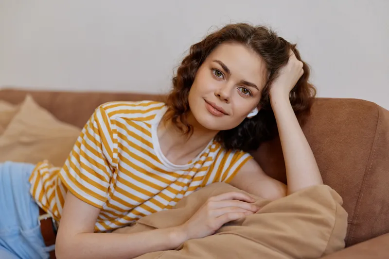 Relaxed woman lounging on a sofa in a striped t shirt, warm neutral living room, casual lifestyle scene conveying comfort, ease, and everyday moments at home