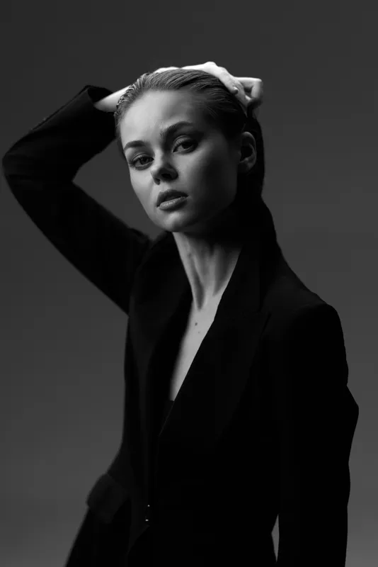 Black and white portrait of a young woman in a dark blazer with serious expression and hand in hair.