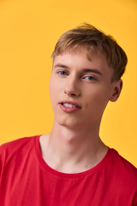 Close up of a young man wearing a red shirt against a vivid yellow background, showcasing casual style, relaxed mood, and bright color harmony for lifestyle imagery.