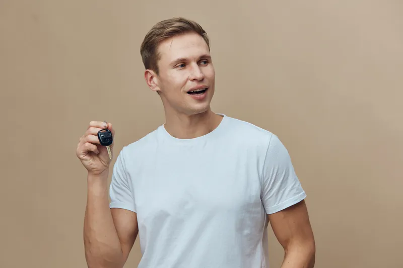 smiling young caucasian man hold smart key fob wearing white t-shirt look aside isolated on beige background cyber security concept