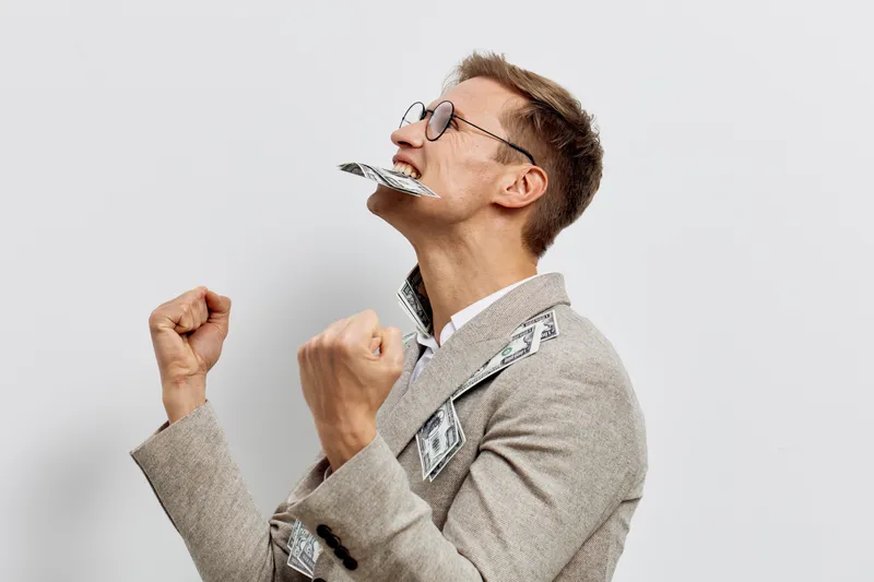 Confident man in glasses dressed in suit celebrating with dollar bills flying around isolated on plain white background studio portrait. Success wealth concept