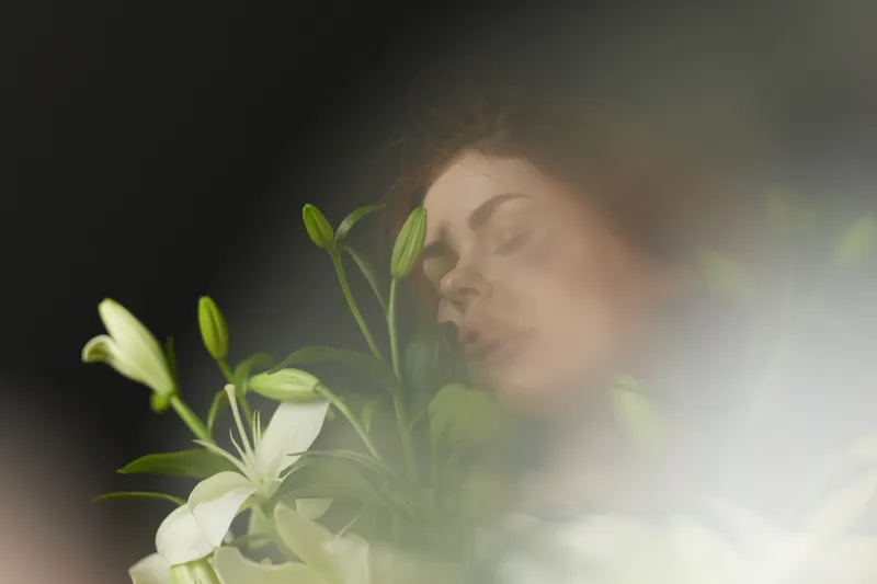 A serene young woman with curly hair surrounded by white lilies, conveying peace and tranquility in a soft, ethereal atmosphere, ideal for wellness concepts