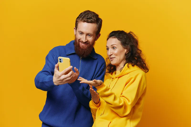 Счастливая пара — мужчина и женщина — улыбаются, держа в руках телефон и просматривая фотографии и видео в социальных сетях