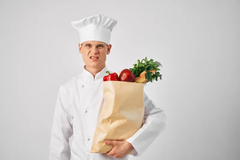 Мужчина в поварской форме держит упаковку продуктов, работа в сфере обслуживания
