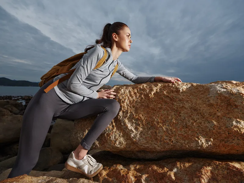 Young female hiker in athletic clothing, contemplating nature on rocky coastline, showcasing determination and adventure, perfect for outdoor lifestyle themes