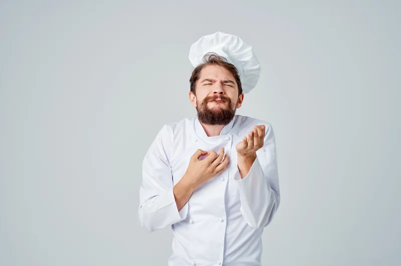 Бородатый мужчина-шеф-повар занимается кулинарией, демонстрируя профессиональные эмоции