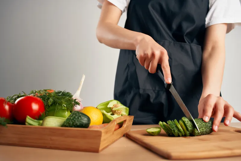 Женщина в чёрном фартуке нарезает овощи на кухне, готовит еду