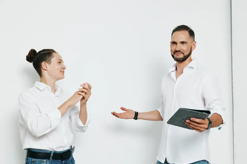 Professional businessman and colleague discuss ideas against a clean colored background, conveying confidence, focus, and curiosity through expressive gestures.