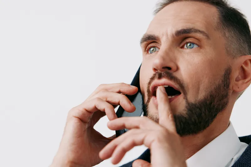 A professional man on a business call, showing surprised yet focused emotion, isolated on a bright clean background, conveying corporate communication and workplace urgency.