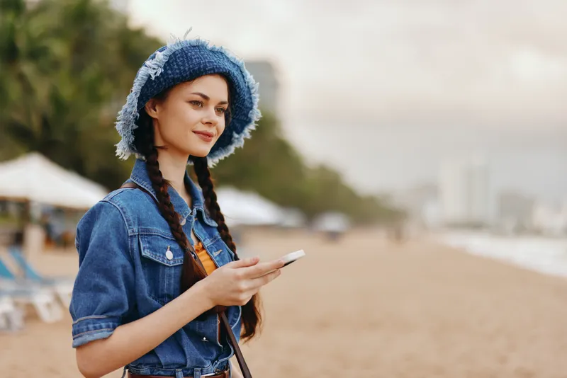 Симпатичная молодая девушка на улице держит смартфон и пользуется приложением для обмена сообщениями во время летнего отдыха в городе