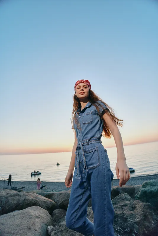lifestyle woman wearing modern boho-western denim outfit on beach rocks during sunset in film color style, casual street fashion with red bandana