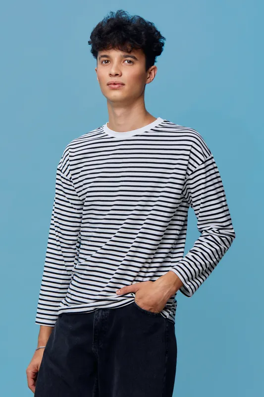 young man in striped long sleeve shirt standing against a blue background, casual style with relaxed posture and curly hair, studio portrait