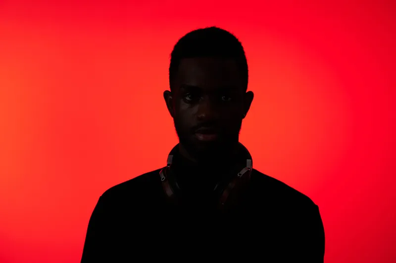 Stylish young Black man with headphones against a vibrant red background, expressing mystery and allure through his silhouette during a night setting
