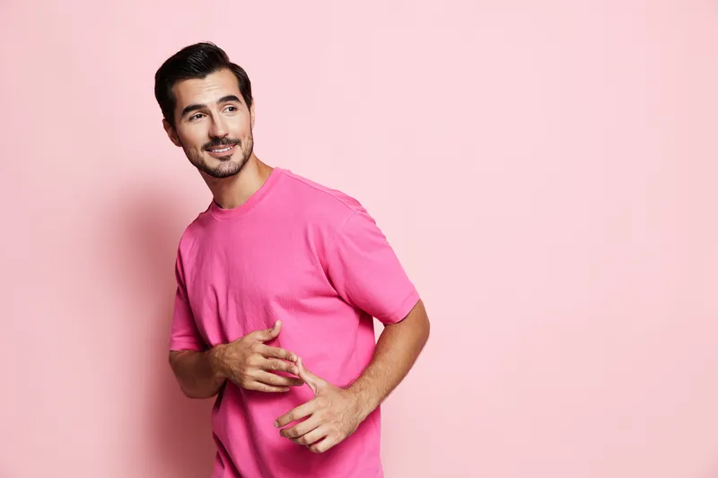 Handsome smiling man wearing a vibrant pink t-shirt poses confidently against a solid pink background. Expressing joy and charm with casual style and cheerful demeanor.